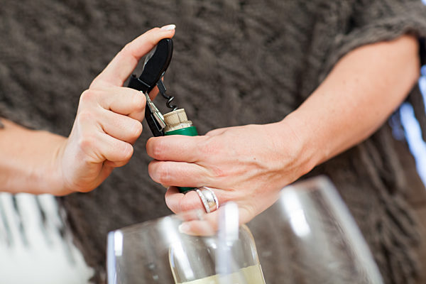 Eine Frau oeffnet Weissweinflasche