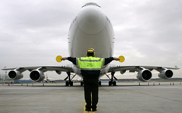 Ein Mitarbeiter der Vorfeldaufsicht weist mit gelben Kellen ein Flugzeug zu...