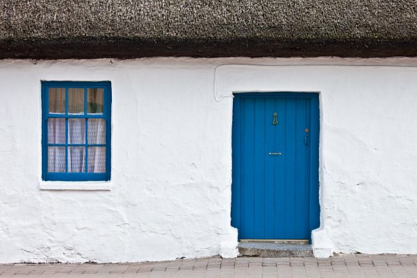 Blue and white traditional whitewashed thatched cottage in Ardmore Village, County Waterford, Ireland