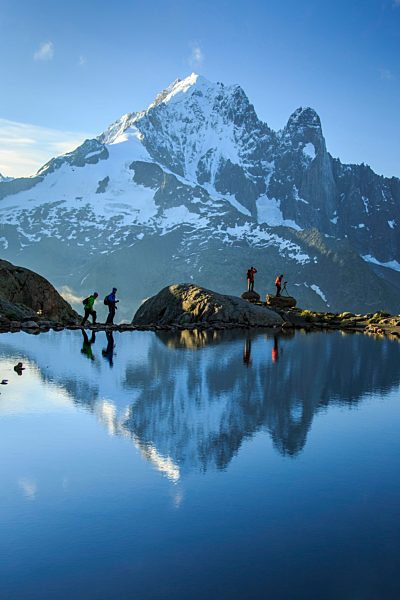 Hikers on the shores of Lac de Cheserys  where Aiguille Verte is reflected at dawn Chamonix Haute Savoie France Europe