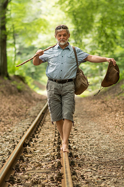 Rentner wandert mit Stock und Hut auf Gleise