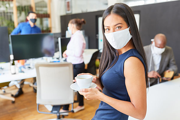 Business Frau mit Kaffeetasse und Mundschutz im Büro