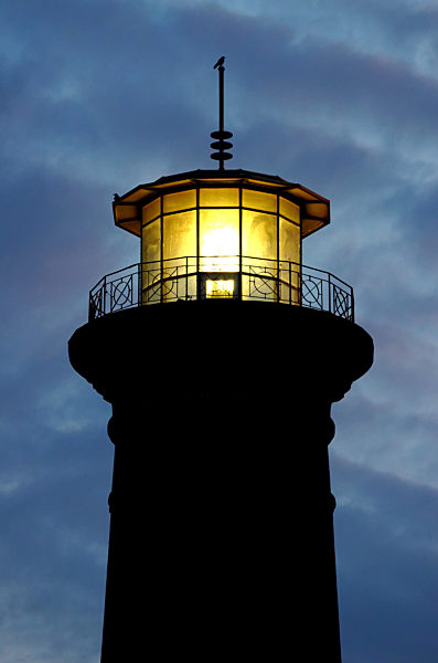 beleuchtete Leuchtturmspitze in der Dämmerung vor einem tiefblauen Abendhimmel