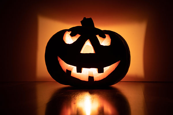 halloween pumpkin with smiling face on fir branches, four teeth. light illuminating the pumpkin from inside