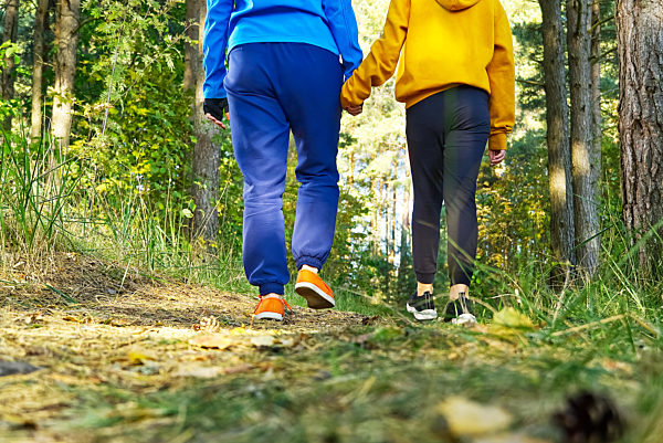 Mom with daughter walking in nature on the forest road holding hands. Mother with daughter hiking in autumn pine forest.
