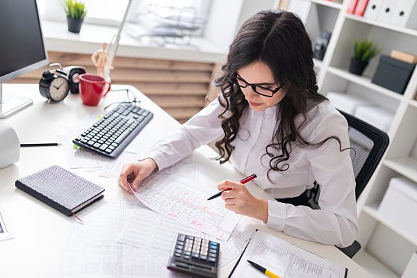 Young girl sits at office desk and fills documents with her left hand.