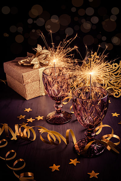 New Years Eve home setting table with sparklers in wine glass with gift box and carnival mask