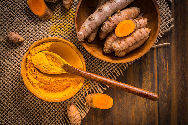 Turmeric root and powder (Curcuma longa) as cooking ingredient on wooden background