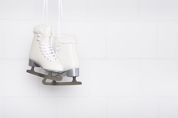 Pair of white figure skates for females hanging at a white concrete background with space for copy