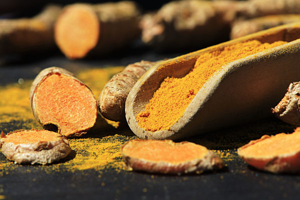 Turmeric powder in a wooden spoon and roots on a dark table (curcuma longa), Kurkuma