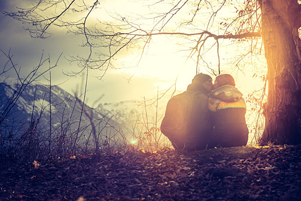 Idyllic mountain sundown scenery: Young sitting couple enjoys the view