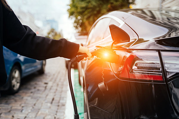Woman near electric car. Vehicle charged at the charging station.