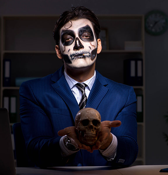 Businessman with scary face mask working late in office