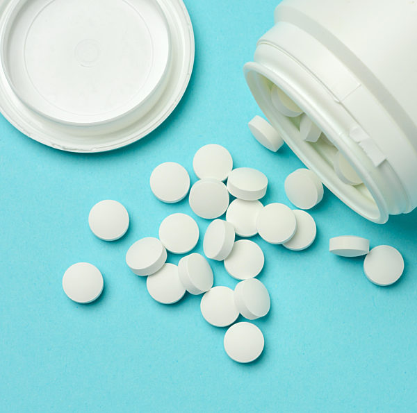 round white pills spilled out of a plastic jar on a blue background