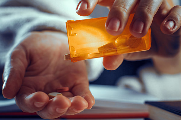 Close up look of hands while pouring the pills out of the bottle.