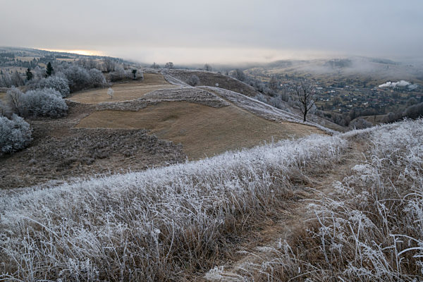 Winter coming. Picturesque pre sunrise scene above late autumn mountain countryside with hoarfrost on grasses, trees, slopes. Peaceful sunlight rays from cloudy sky. Ukraine, Carpathian Mountains.