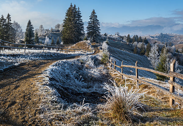 Winter coming. Last days of autumn, morning in mountain countryside peaceful picturesque hoarfrosted scene. Dirty road from hills to the village. Ukraine, Carpathian mountains.