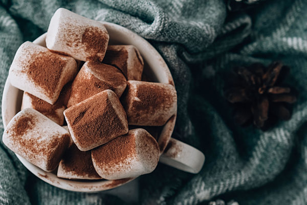 Cocoa drink with marshmallow and cacao powder on cozy winter sweater background. Christmas lights. Winter holiday home atmosphere