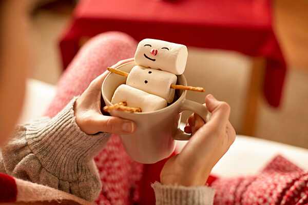 hands with marshmallow snowman in mug on christmas