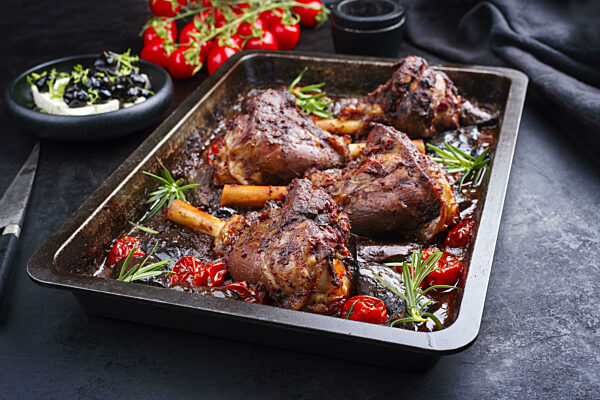 Traditional braised slow cooked Greek lamb shank in red wine sauce with eggplants and tomatoes served as close-up in a backing form