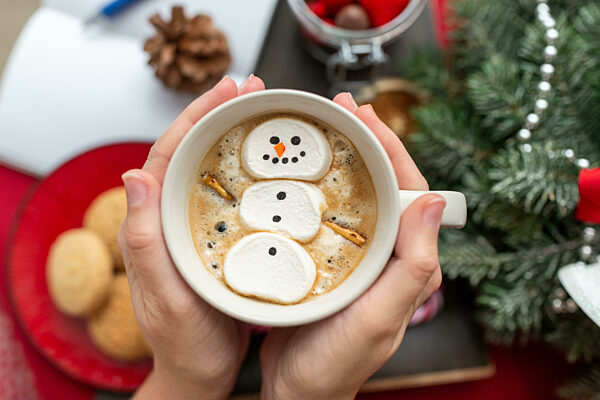 hands with marshmallow snowman in mug on christmas