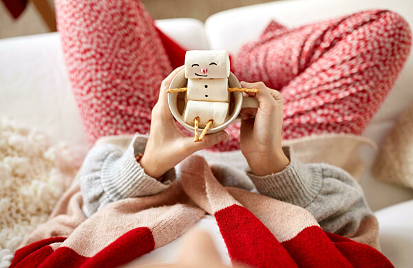 hands with marshmallow snowman in mug on christmas