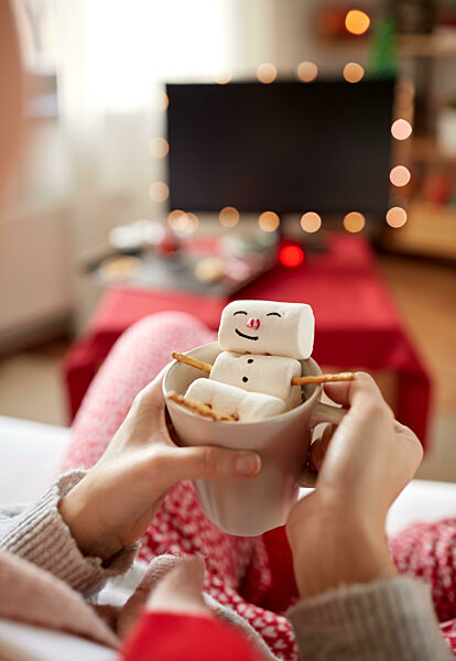 hands with marshmallow snowman in mug on christmas