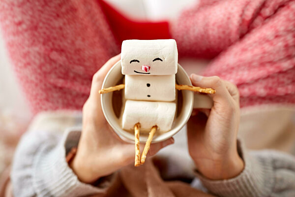 hands with marshmallow snowman in mug on christmas