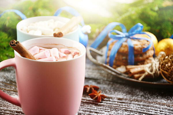 Christmas background of two mugs of hot chocolate with marshmallows, spruce branch and tray with gingerbread cookies on wooden table