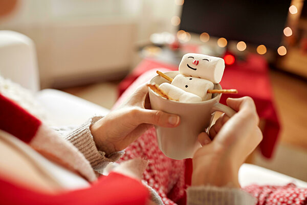 hands with marshmallow snowman in mug on christmas