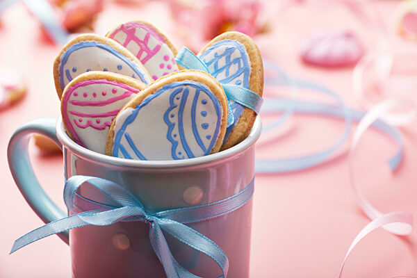 Easter baking background of frosted cookies in shape of egg in blue mug on pink background