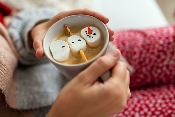 hands with marshmallow snowman in mug on christmas