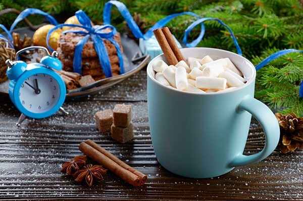Christmas background of blue hot chocolate mug with marshmallows, spruce branch alarm clock and tray with gingerbread cookies on wooden table