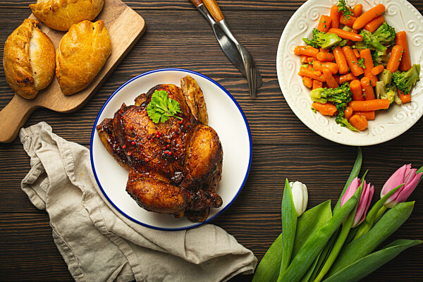 Easter food on dark rustic table: pastel colored eggs, roasted chicken, vegetables, buns