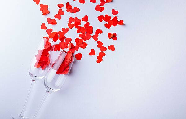 Champagne flutes with red heart shapes scattered by copy space over white background