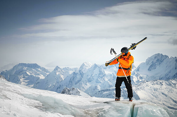 Portrait of a young skier with skis on his shoulder. It stands high in the mountains on a glacier against the backdrop of high mountains. The concept of freeride and backcountry in the highlands