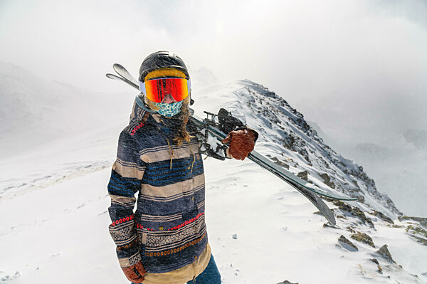 Portrait of a pretty and active woman skier, wearing a mask and holding skis in her hands, active winter holidays