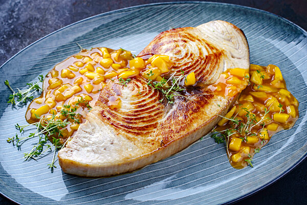 Fried swordfish steak with mango chutney and herbs served as close-up on a Nordic design plate