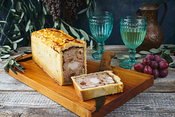 Traditional French Pate en croute with rabbit meat and pork filet served with grapes as close-up on a modern design wooden board