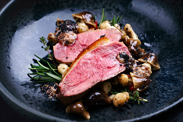 Barbecue gourmet duck breast filet served with mushrooms and truffle cream as close-up on a design plate