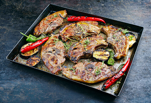 Barbecued lamb saddle back chop steaks with chili and eggplants served as close-up on a rustic metal sheet