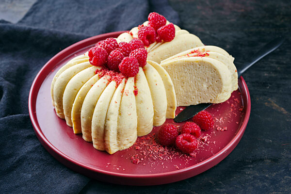 Traditional Italian vanilla cheese cake with fresh raspberries served as close-up on a red design plate
