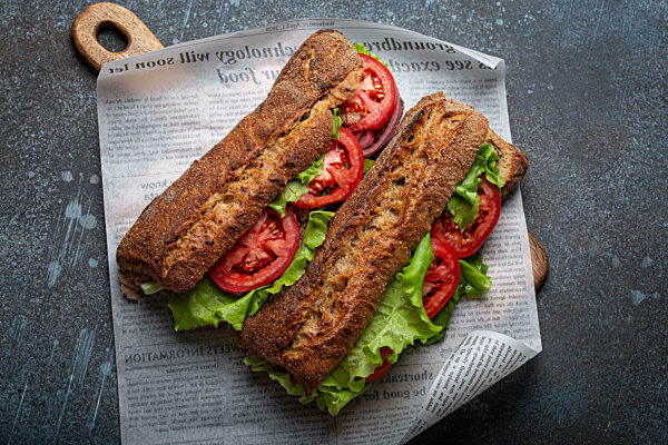 Two dark ciabatta sandwiches with green salad, ripe red tomatoes, onion and tuna