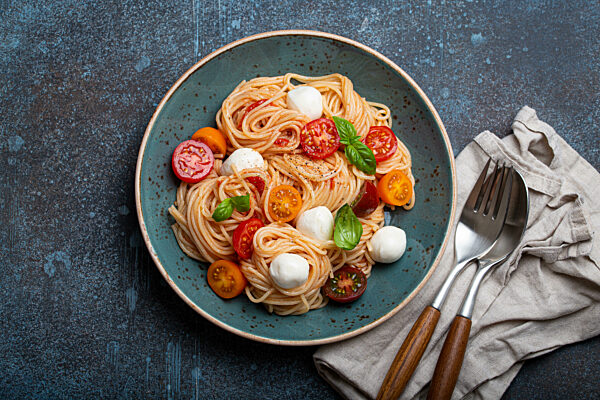 Spaghetti with mozzarella, colourful cherry tomatoes, fresh basil on ceramic plate