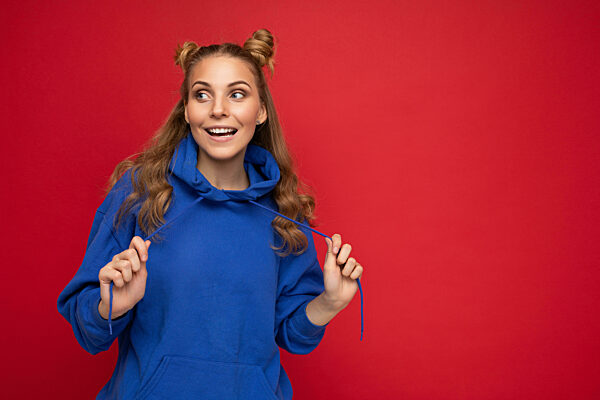 Photo of young charming beautiful attractive happy smiling delightful blonde woman with two horns with sincere emotions wearing stylish hipster blue hoodie isolated over red background with copy space