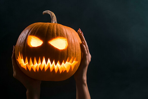 Pumpkin face with candle light inside in smoky dark backdrop, trick or treat. Halloween party decoration. Scary symbol Jack-o-lantern expression on left side of frame. Copy space