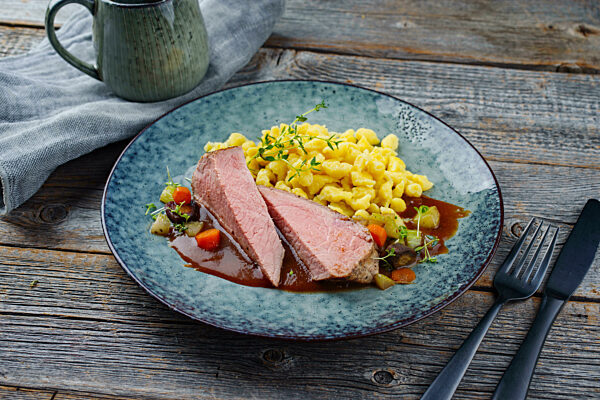 Tafelspitz roast veal slices with Swabian spaetzle and vegetable served with dark beer sauce as close-up on a Nordic design plate