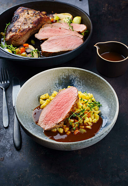 Tafelspitz roast veal slices with Swabian spaetzle served with dark beer sauce as close-up in a design bowl and pot