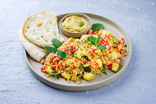 Traditional Moroccan vegetable couscous with pita bread and hummus served as close-up on a Nordic Design plate