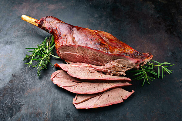 Traditional barbecue leg of venison sliced and served with herbs as close-up on rustic black board with copy space